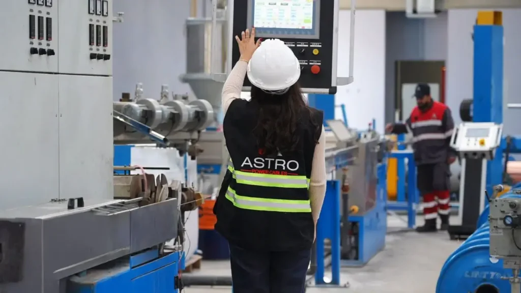 Worker operating Astro Cables extrusion machine control panel.